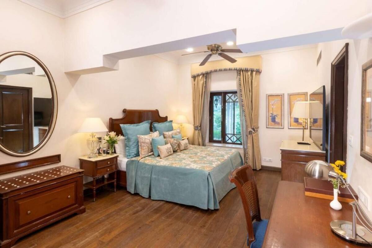 Un dormitorio con cama, mesitas de noche, cómoda, espejo y ventana con cortinas.