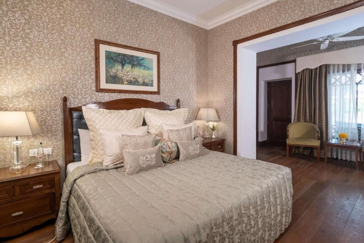 Un dormitorio con una cama grande, una mesita de noche con lámpara, un cuadro en la pared y una silla en la esquina.