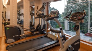 Un gimnasio con varias máquinas de ejercicio, incluyendo cintas de correr y elípticas, con vistas a árboles.