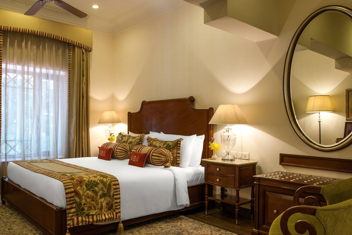 Una habitación de hotel con una cama grande, dos mesitas de noche, un espejo y vistas al exterior a través de una ventana con cortinas.