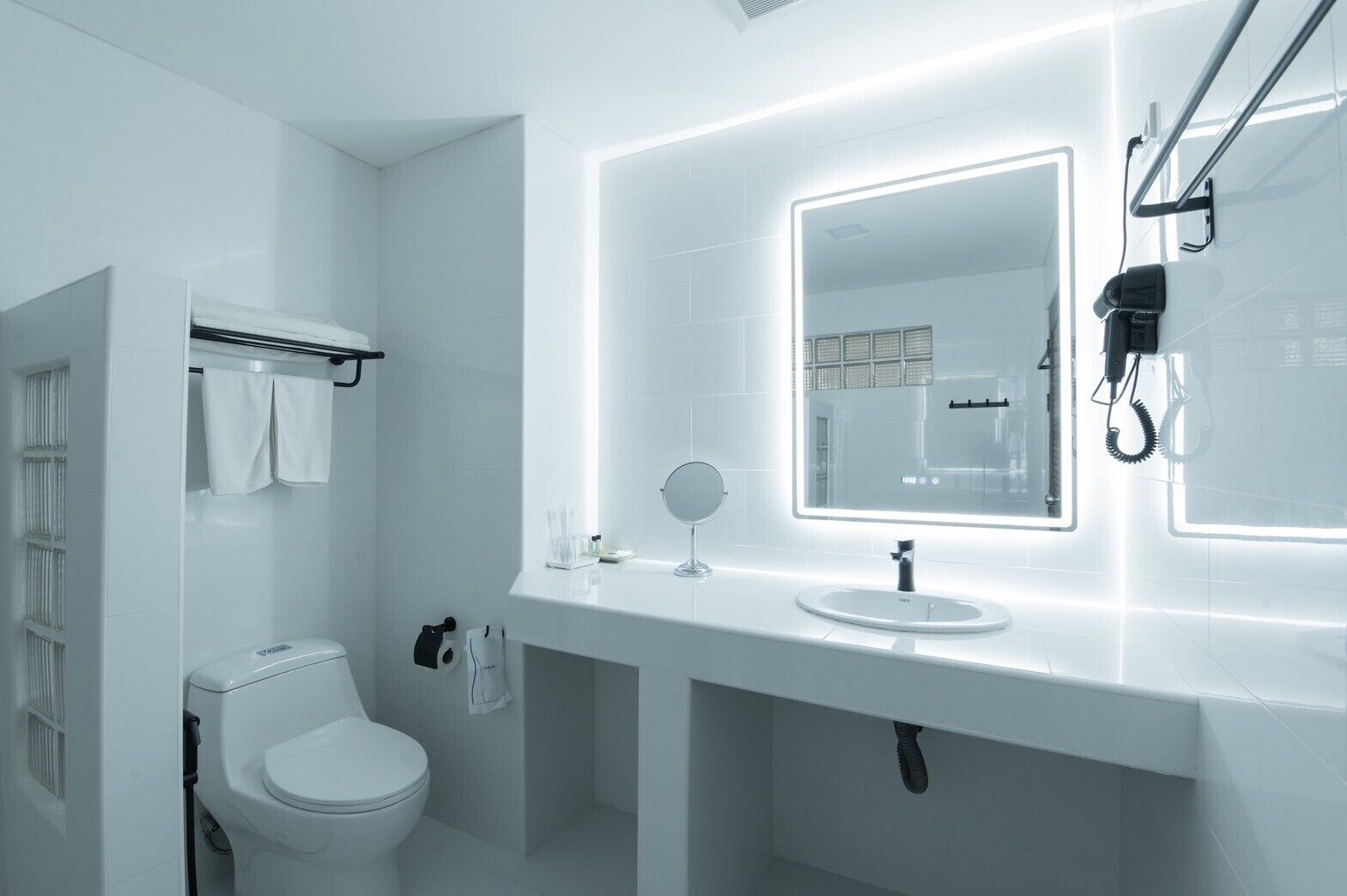 Un baño moderno con inodoro blanco, lavabo con espejo y un perchero para toallas.
