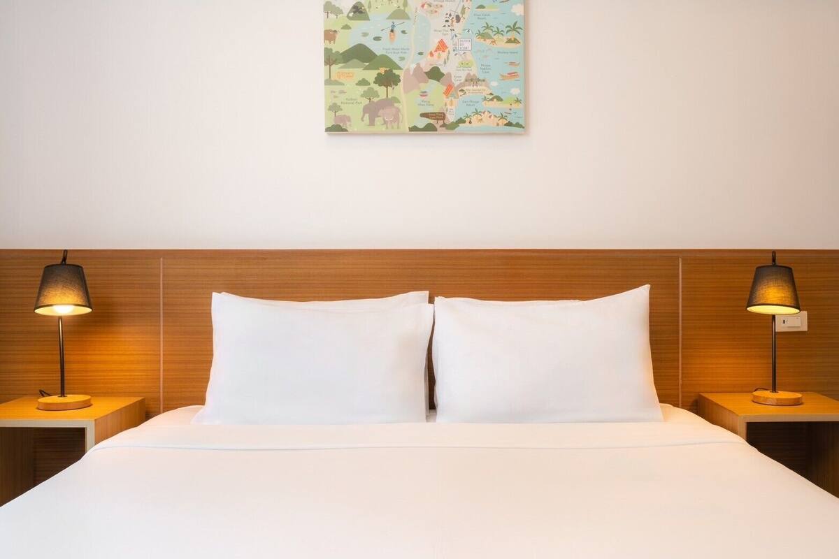 A hotel room with a wooden headboard, two white pillows, and a wall-mounted map.
