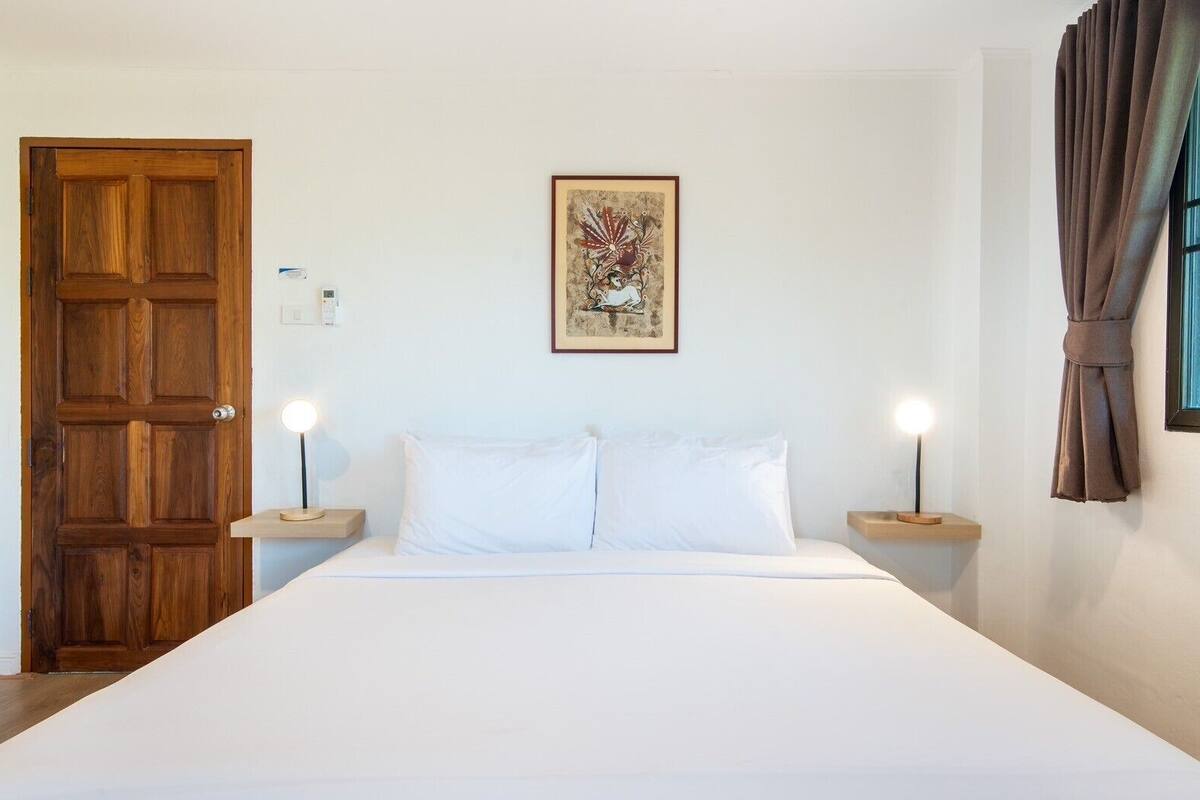A hotel room with a large bed, two bedside tables with lamps, a wooden door, and a framed picture on the wall.