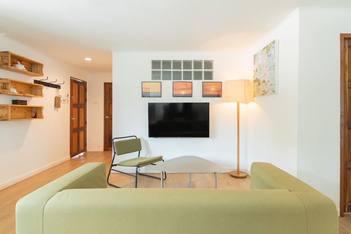 A living room with a green sofa, a chair, a flat-screen TV, and a floor lamp.