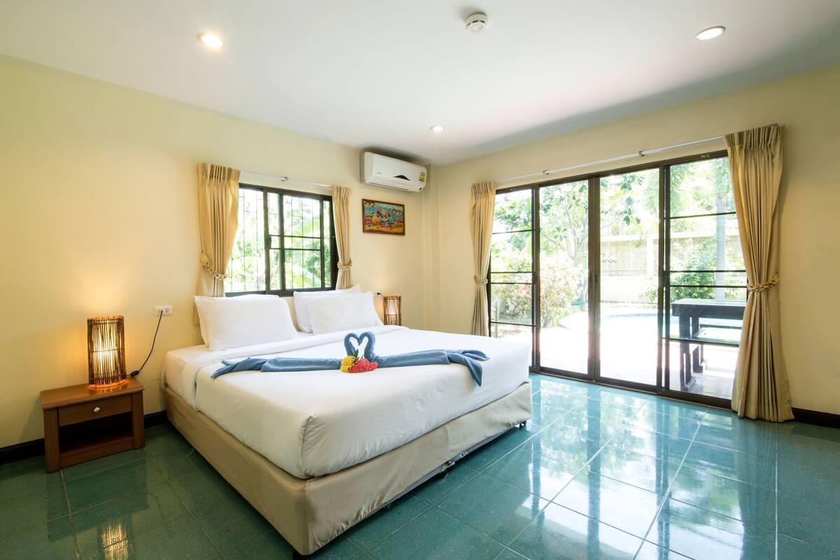 A hotel room with a large bed, a nightstand, a lamp, and a view of the outdoors through large sliding glass doors.
