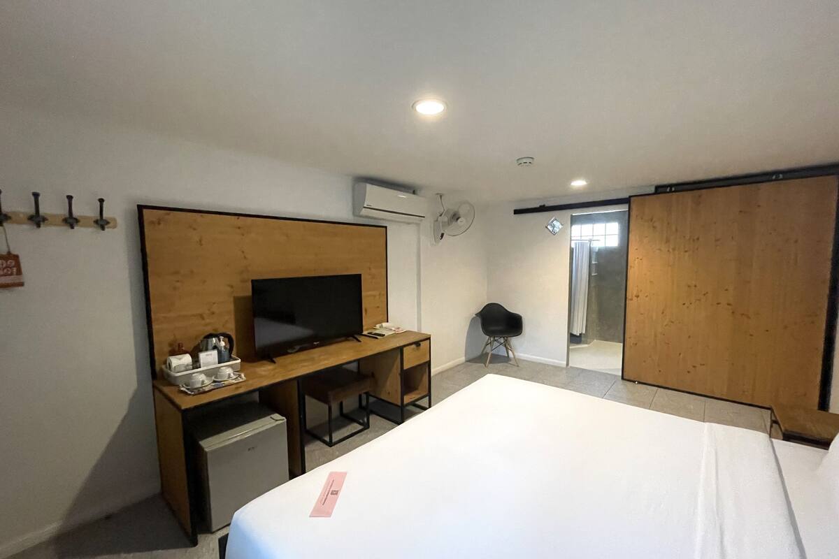 Ett hotellrum med en säng, ett skrivbord med en tv, en stol, ett litet bord och en garderob.