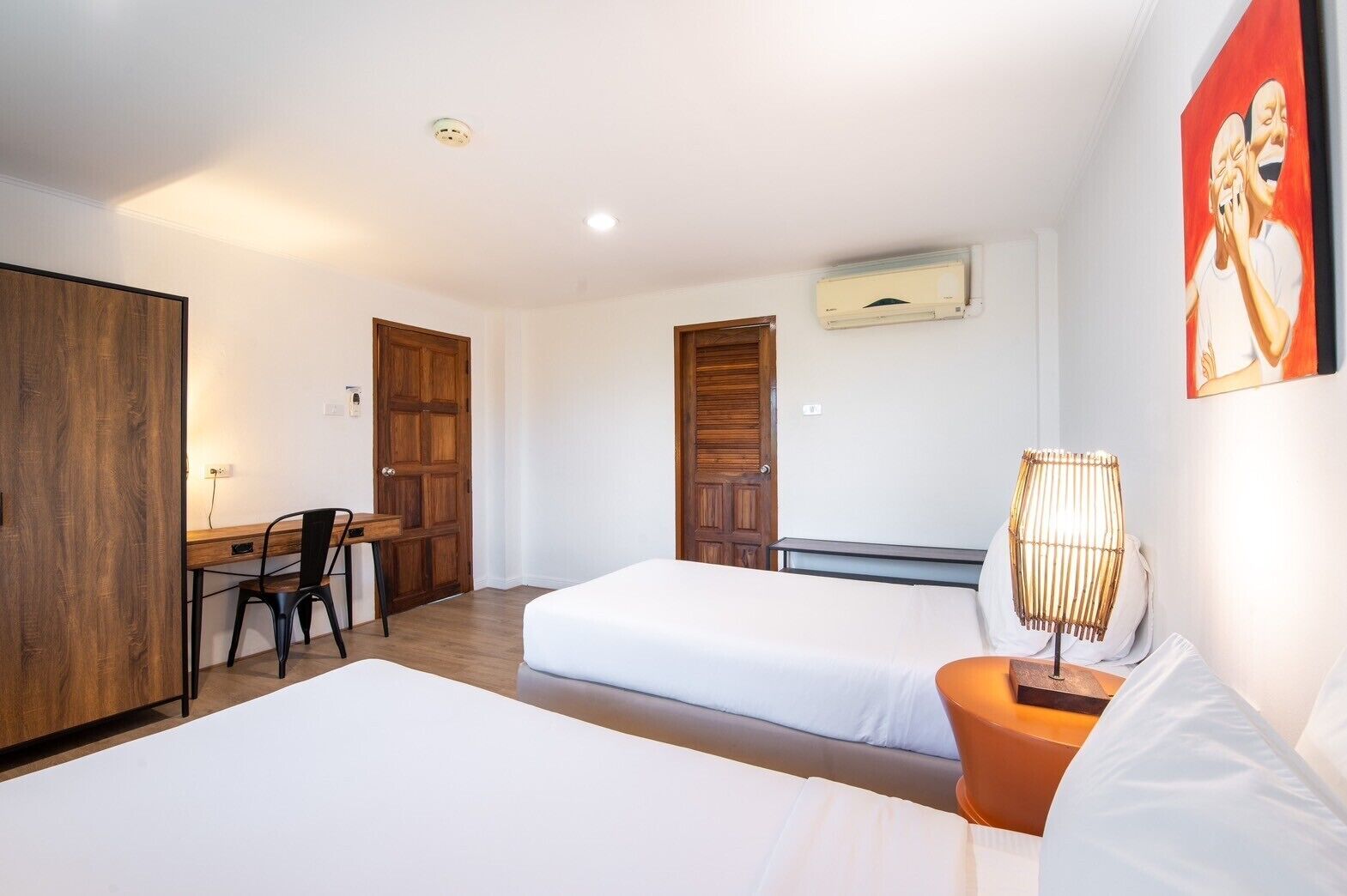 A hotel room with two beds, a desk, a chair, and a lamp.