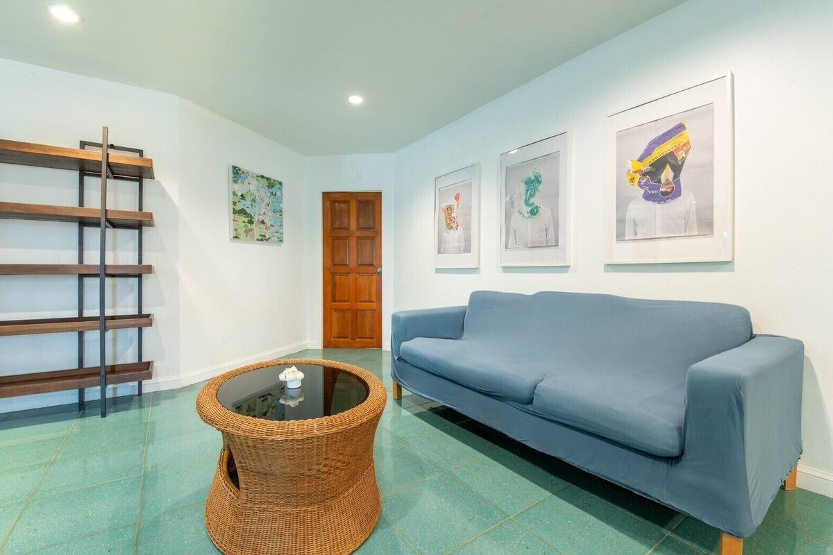 A room with a blue sofa, a wicker coffee table, a wooden ladder, and framed artwork on the wall.