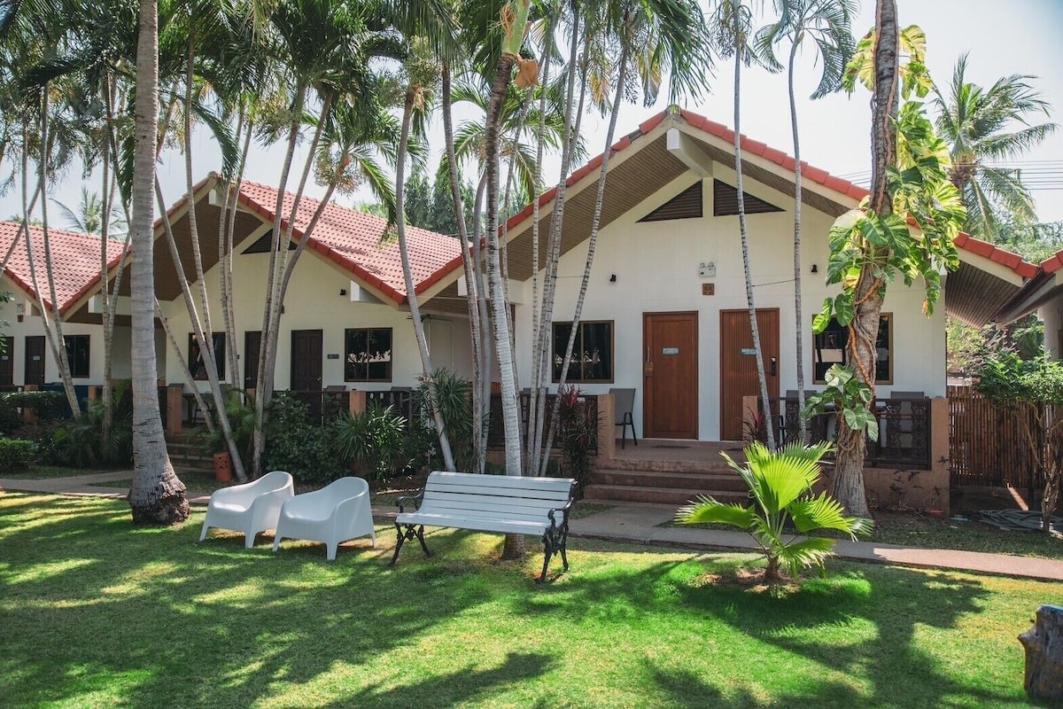 A hotel with a red-tiled roof, white walls, and a small front porch with a bench and chairs.