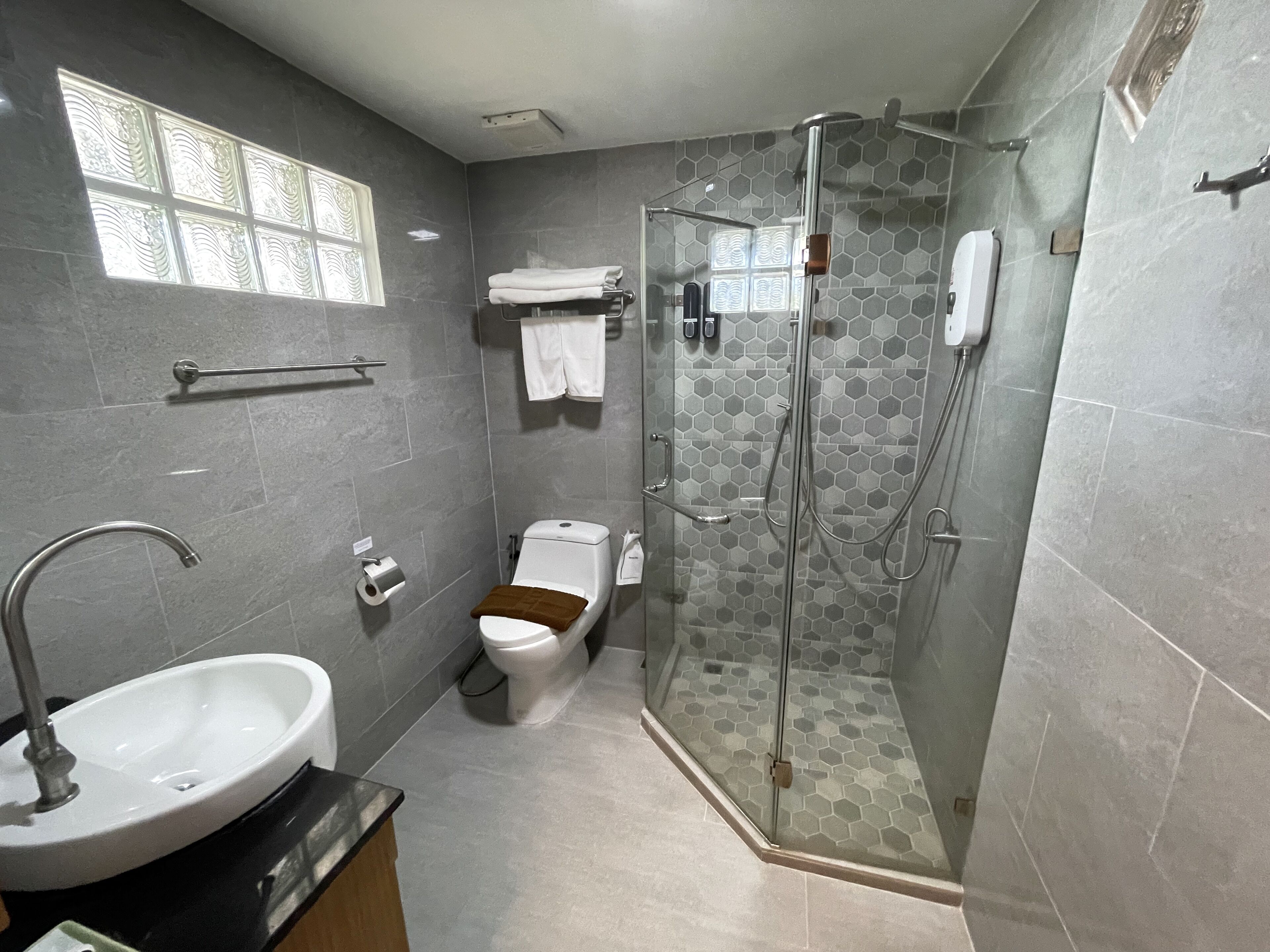 A modern bathroom with a glass-enclosed shower, a toilet, a sink, and a window.