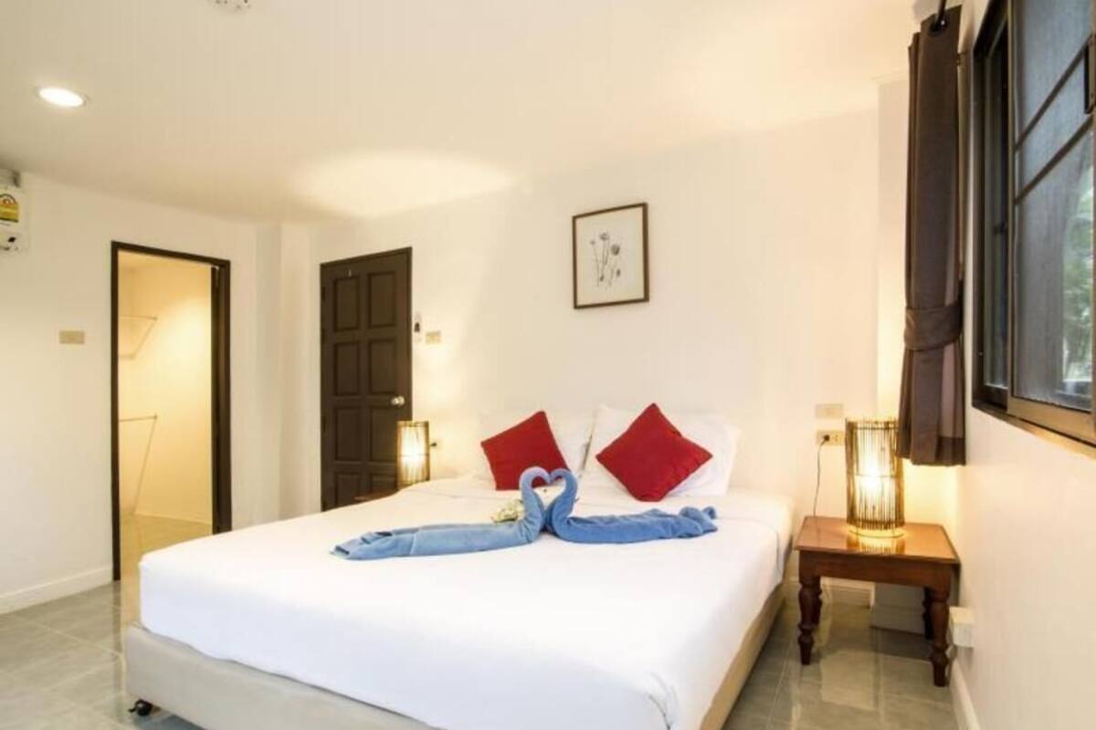 A hotel room with a bed, a bedside table, a lamp, a framed picture on the wall, and a door.