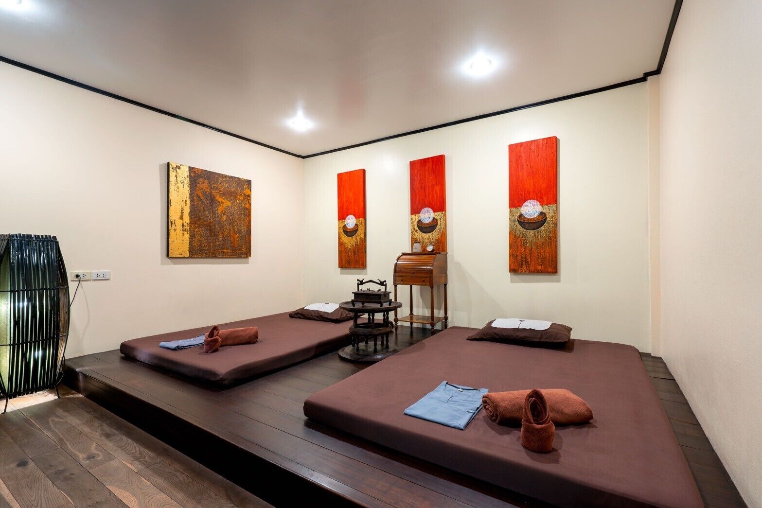 Um quarto com duas macas de massagem, uma mesa pequena e uma cadeira.