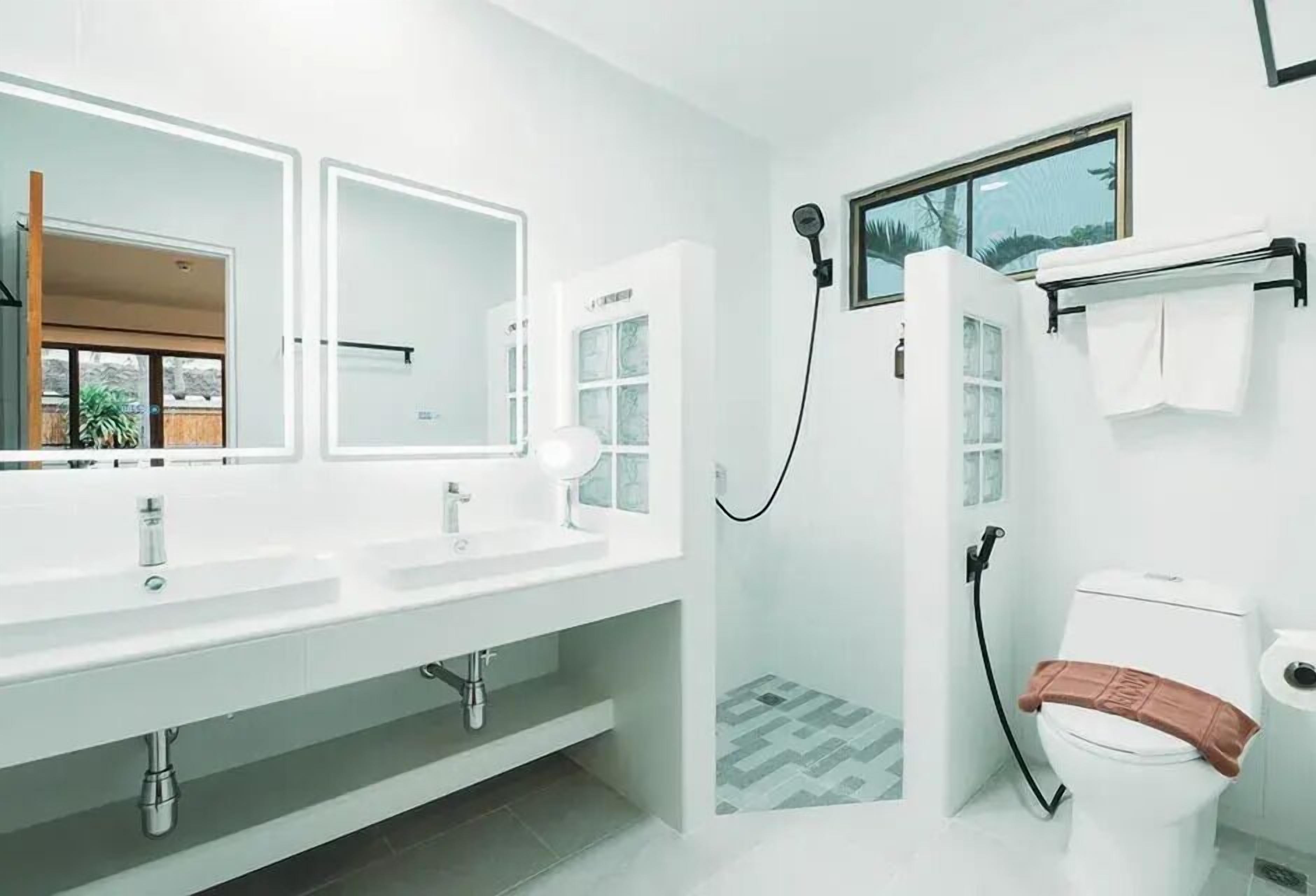 A modern bathroom with a large mirror, two sinks, a shower, and a toilet.