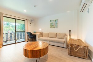 Una sala de estar con un sofá, una mesa redonda de madera, una cesta de mimbre, un ventilador y un escritorio con una silla.