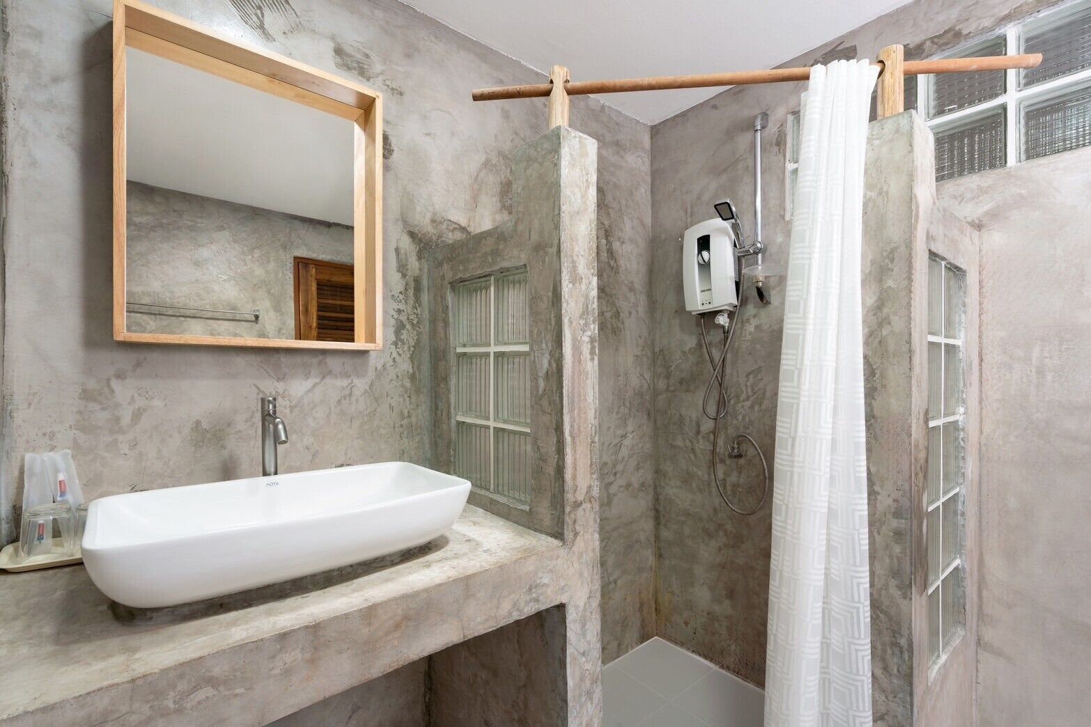 Een badkamer met een grote witte wastafel, een spiegel en een douche met een houten douchetuit.