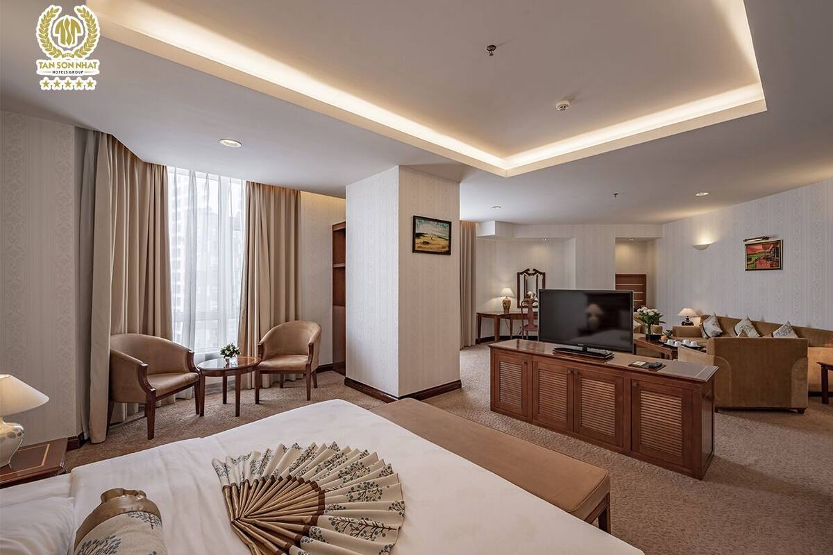 Een hotelkamer met een groot bed, een televisie, een zithoek met een bank en stoelen, en een kleine tafel met een lamp.