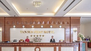 Eine Rezeption im Tan Son Nhat Hotel mit Uhren, die verschiedene Zeitzonen anzeigen, einer Blumenkomposition und einer Kandelaberleuchtre.