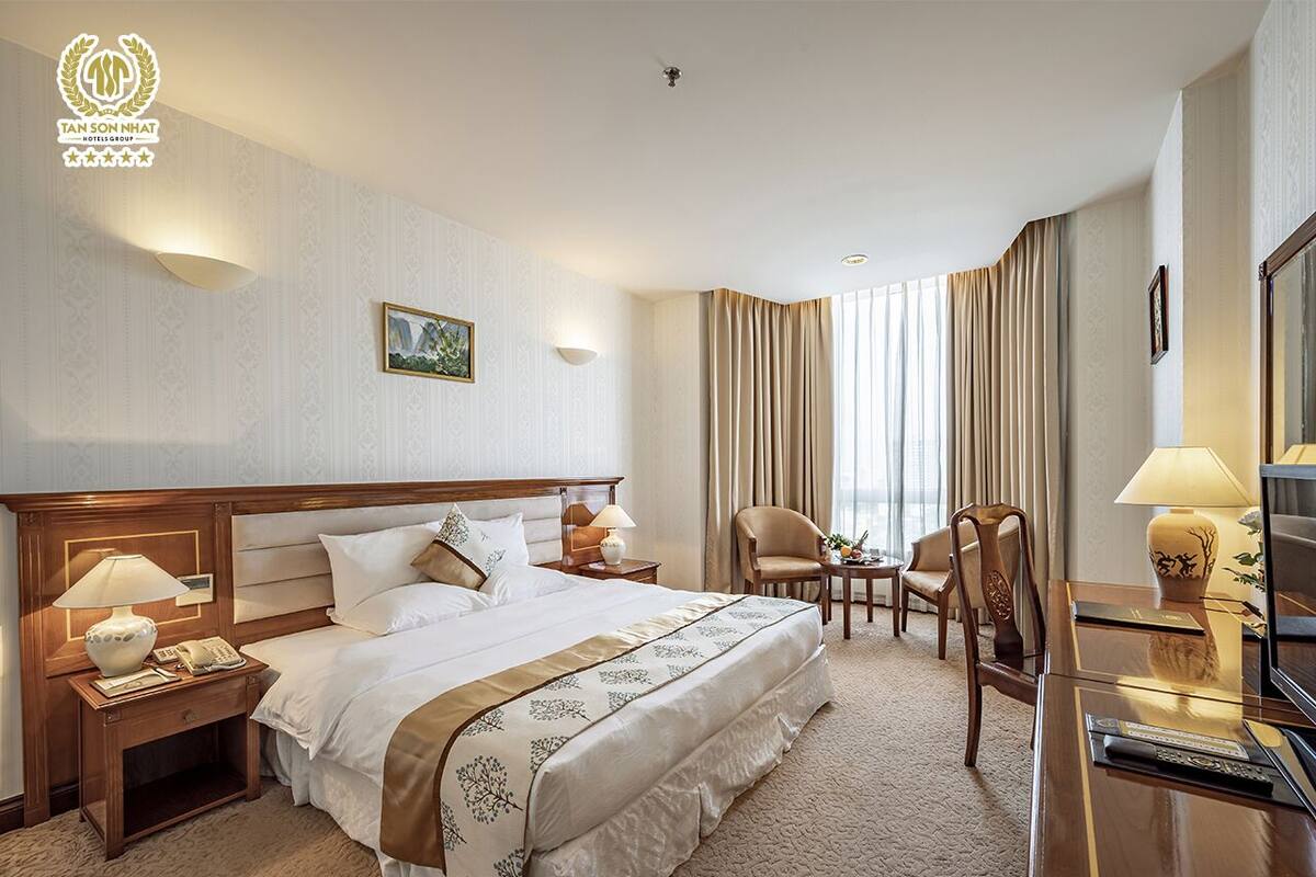 Een hotelkamer met een groot bed, een bureau met stoel, een nachtkastje met lamp en een raam met gordijnen.