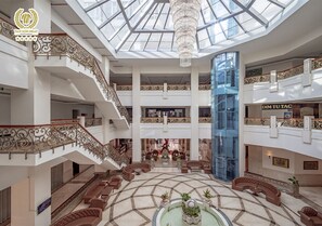 A multi-level atrium with a central seating area, a chandelier, and a glass elevator shaft. - Tan Son Nhat Saigon Hotel (Ho Chi Minh City)