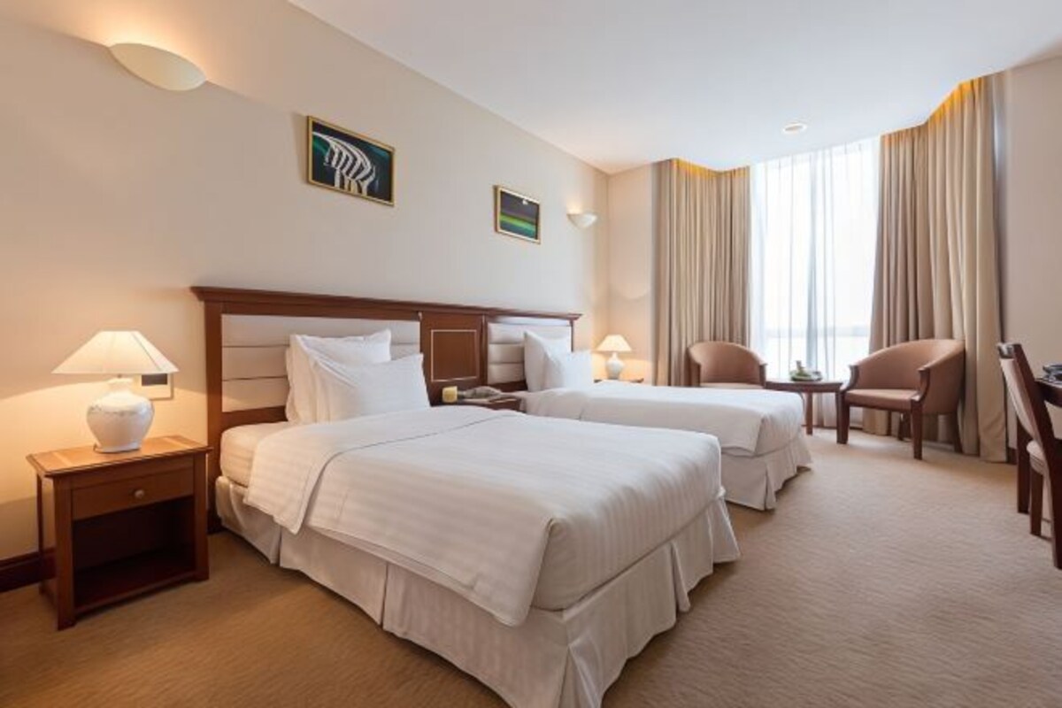 Une chambre d’hôtel avec deux lits, un bureau, une chaise et une fenêtre avec des rideaux.