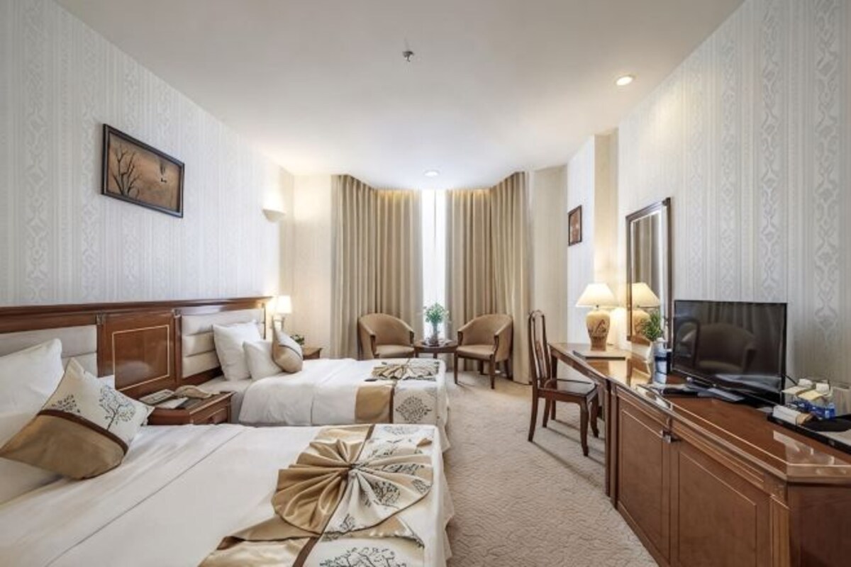 Ein Hotelzimmer mit zwei Betten, einem Schreibtisch, einem Fernseher und einer Sitzecke mit Stühlen.