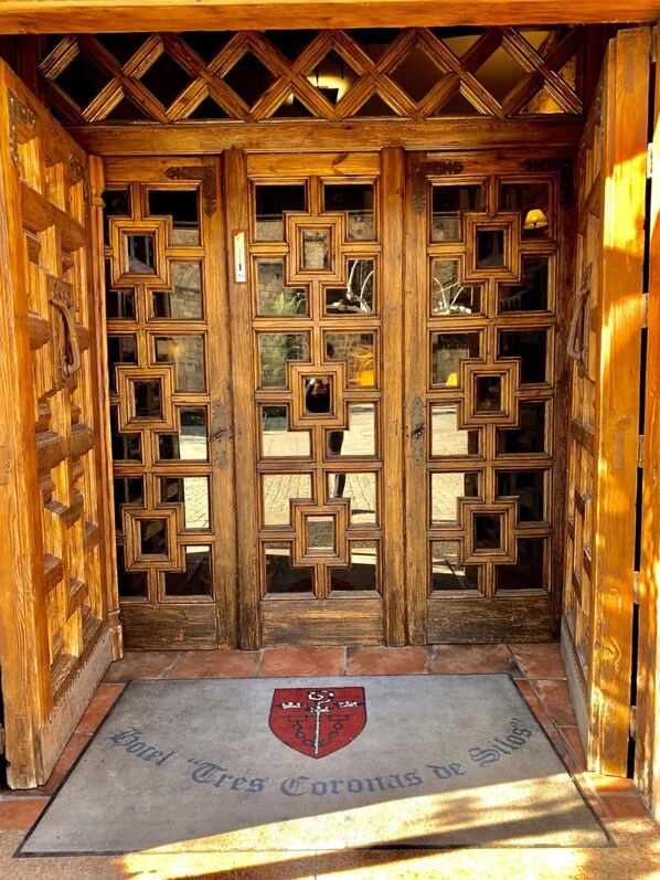 A wooden door with a geometric pattern and a doormat with a coat of arms. - Hotel Tres Coronas de Silos (Santo Domingo de Silos)
