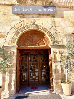 A stone building with a wooden door featuring intricate geometric patterns. A sign above the door reads "Hotel Tres Coronas de Silos." - Hotel Tres Coronas de Silos (Santo Domingo de Silos)