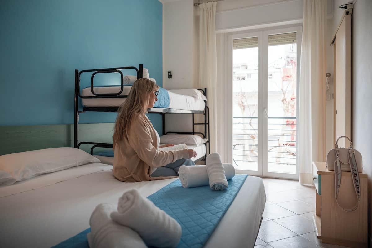 A room with bunk beds, a bed with rolled towels, a wooden nightstand, and a Louis Vuitton bag.