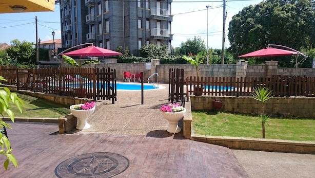 A pool area with two red umbrellas, a wooden fence, and a building in the background. - Hotel Azcona (Noja)