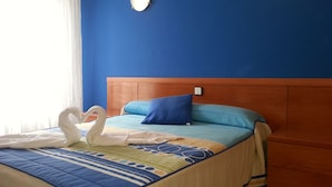 A hotel room with a bed, a wooden headboard, a blue wall, and two wall-mounted lights. - Hotel Azcona (Noja)