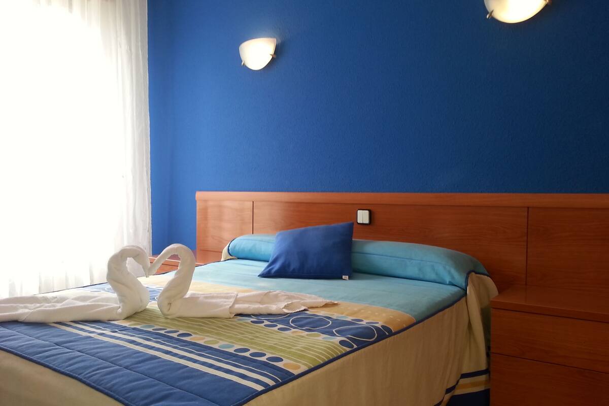 A hotel room with a bed, a wooden headboard, a blue wall, and two wall-mounted lights.