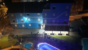 A building with a blue facade, a swimming pool, and a parking area with cars. - Hotel Azcona (Noja)