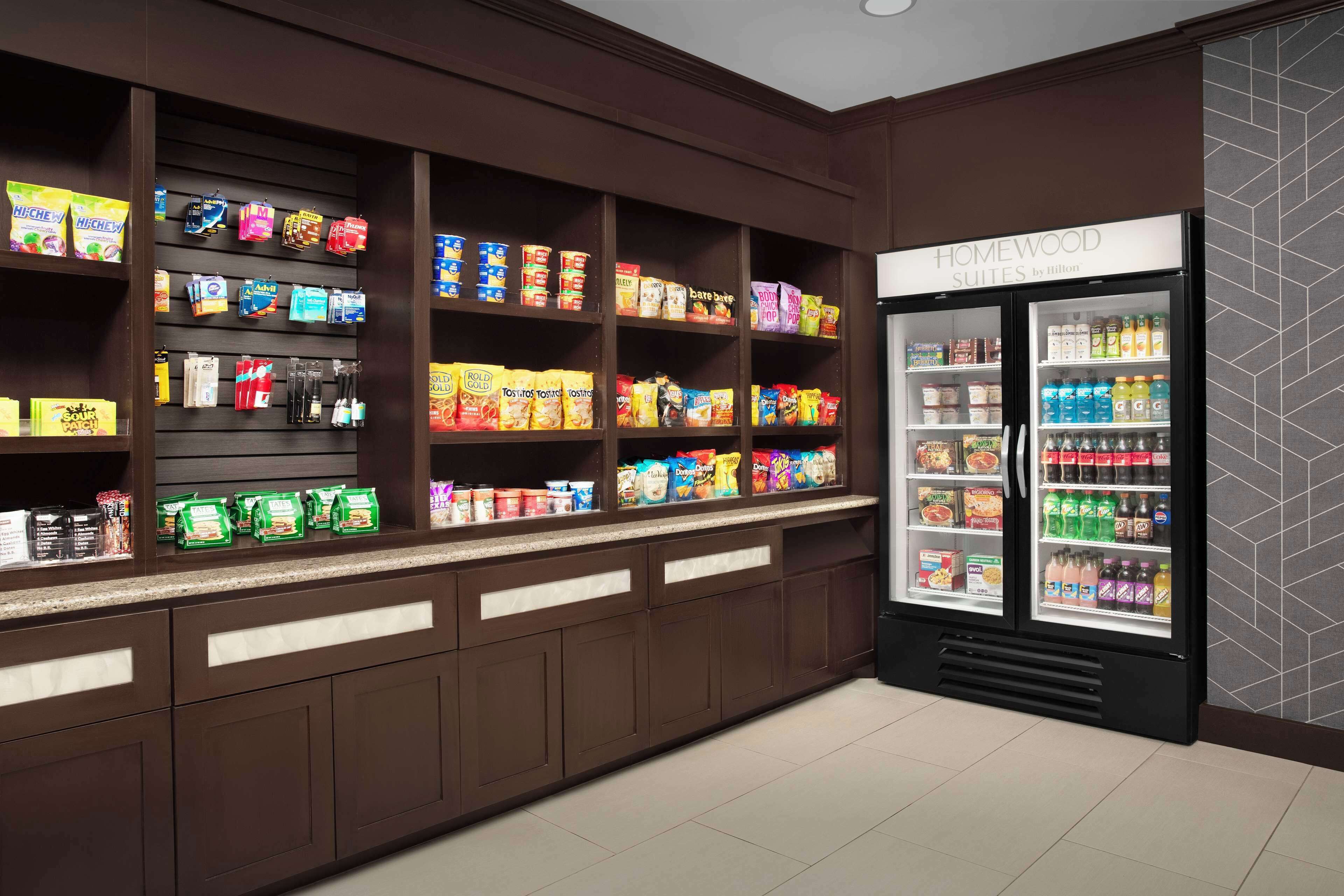 A hotel kitchenette with shelves stocked with snacks and a refrigerator with beverages.