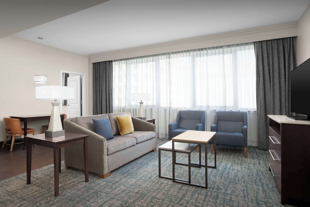 Habitación de hotel con sofá, sillones, mesa de centro, televisor y escritorio con lámparas.