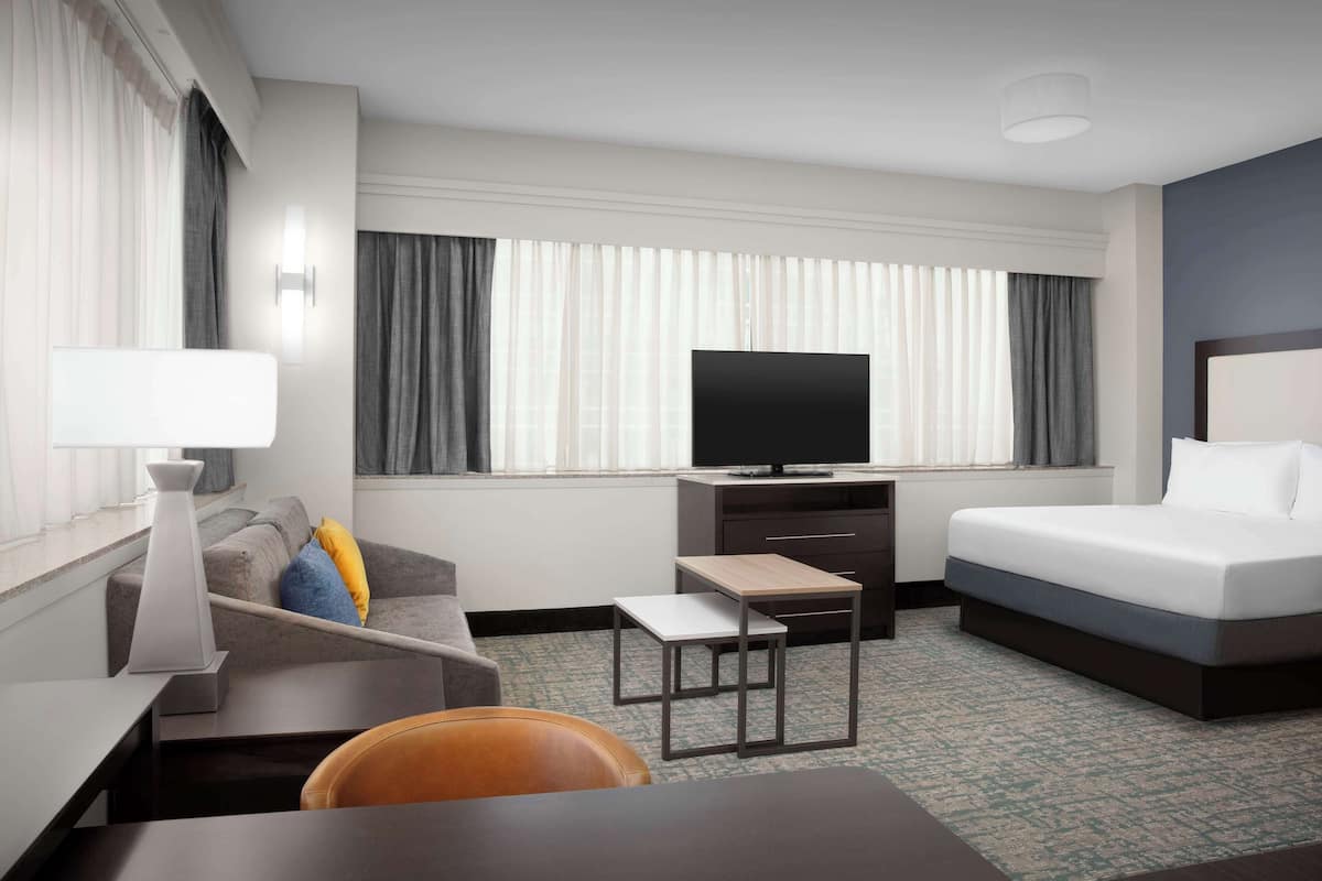 Habitación de hotel con cama, televisión, escritorio, silla y ventana con cortinas.