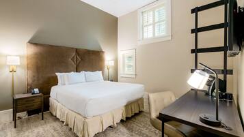 A hotel room with a large bed, bedside tables with lamps, a desk with a chair, and a window with blinds.