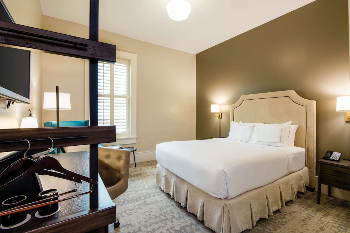 A hotel room with a large bed, a television, a piano, and a desk with a telephone.