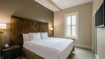 A neatly made bed with white linens, a wooden nightstand with a telephone, and a wall-mounted TV.