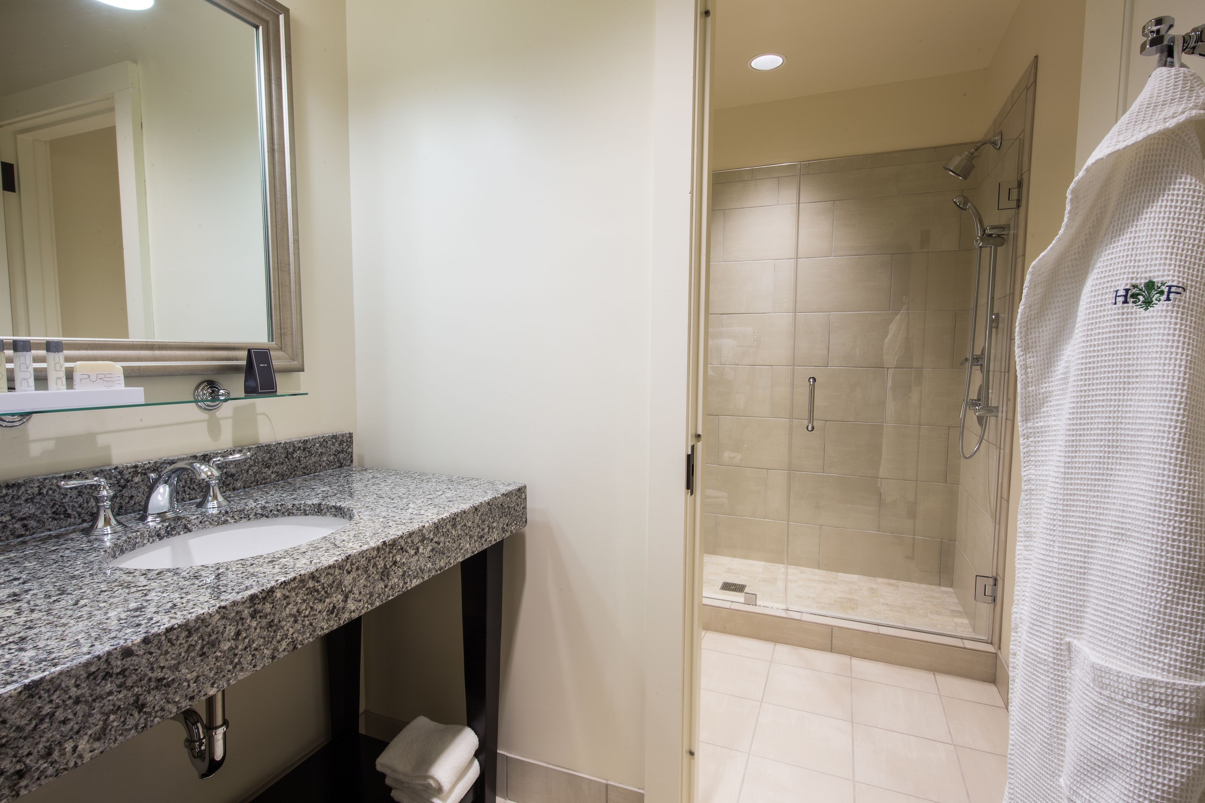 A bathroom with a granite countertop sink, a large mirror, and a glass-enclosed shower area.