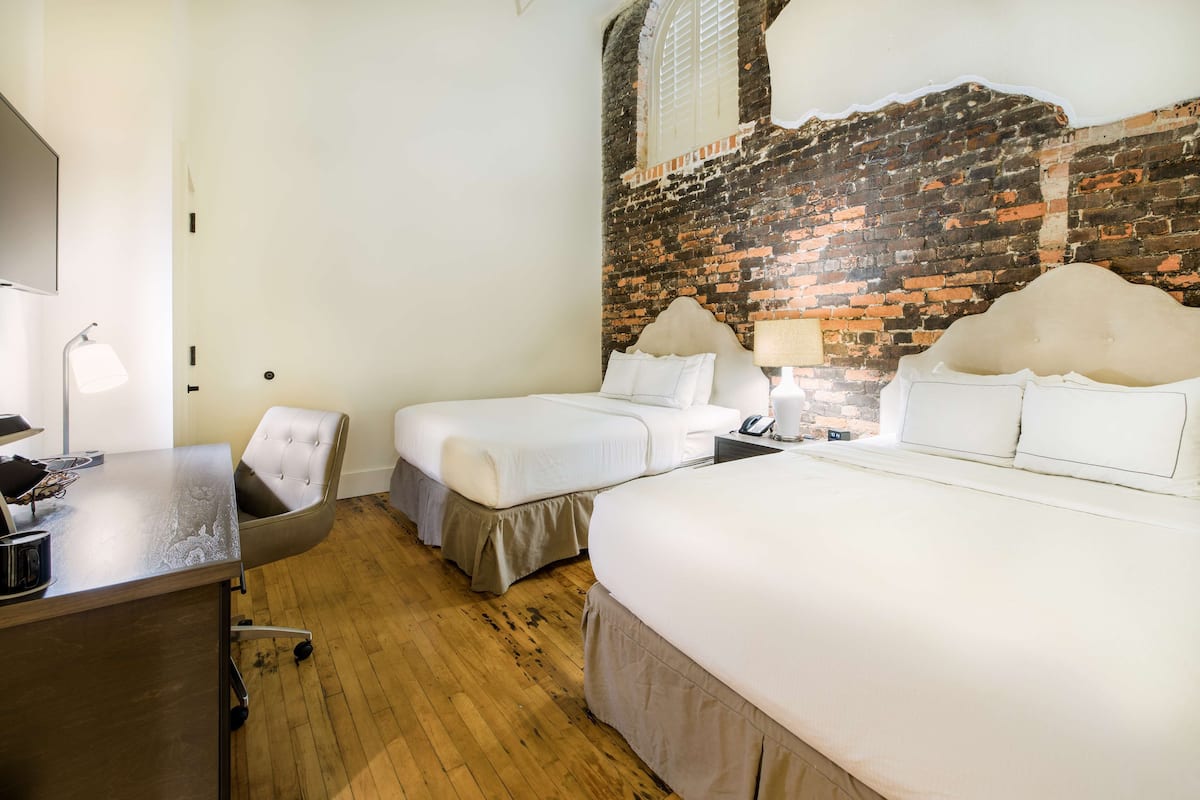 A hotel room with two beds, a desk, a chair, and a brick wall.