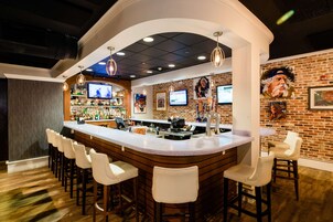 Uma área de bar com balcão curvo, vários bancos e parede de tijolos ao fundo.