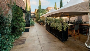 An outdoor patio area with a brick wall, a covered seating area with string lights, and potted plants. - Hotel Florence, Tapestry Collection by Hilton (Florence)