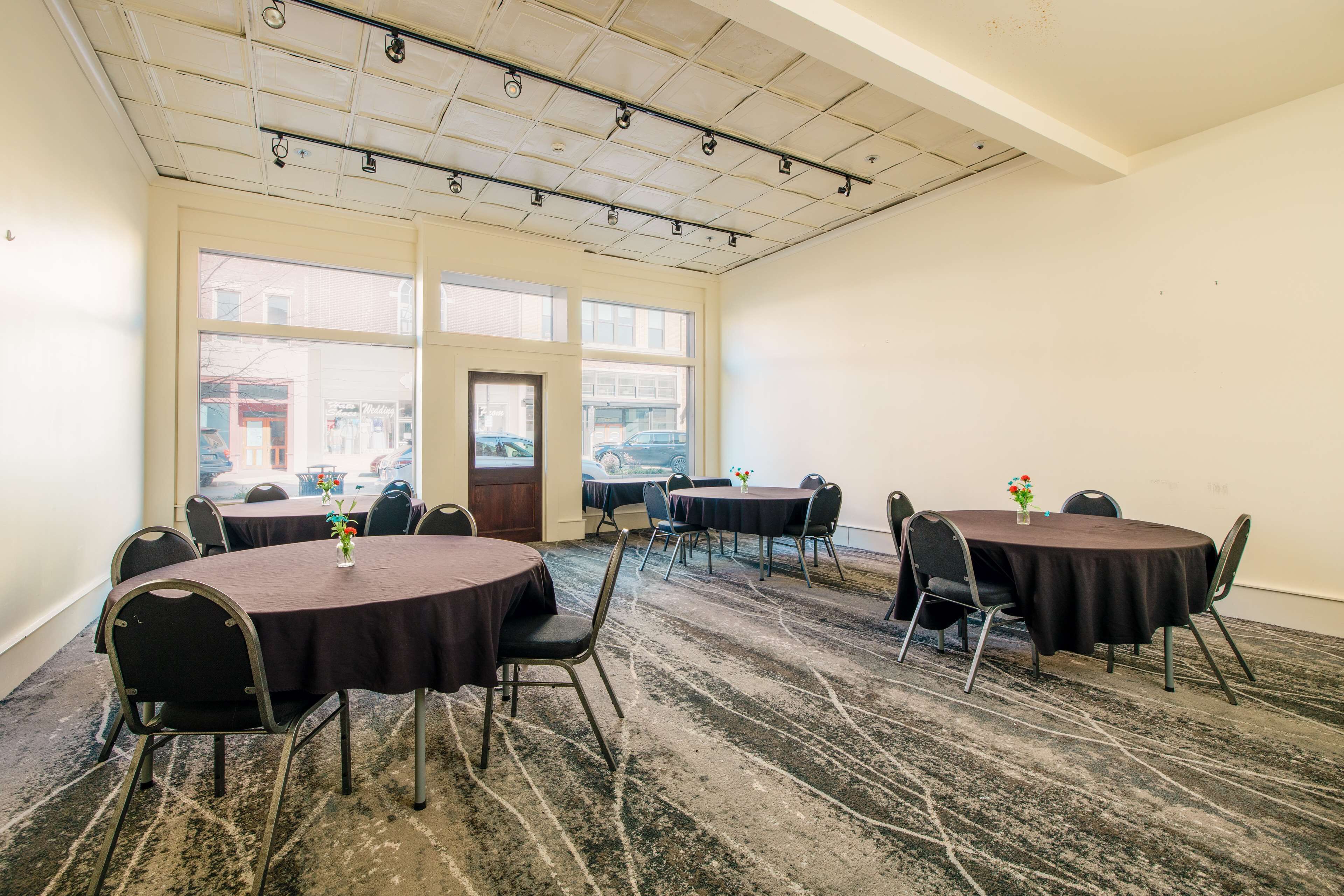 A conference room with multiple tables and chairs, large windows, and a patterned carpet.