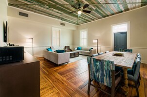 Uma sala de estar espaçosa com piso de madeira, ventilador de teto e uma área de jantar com mesa e cadeiras de madeira.