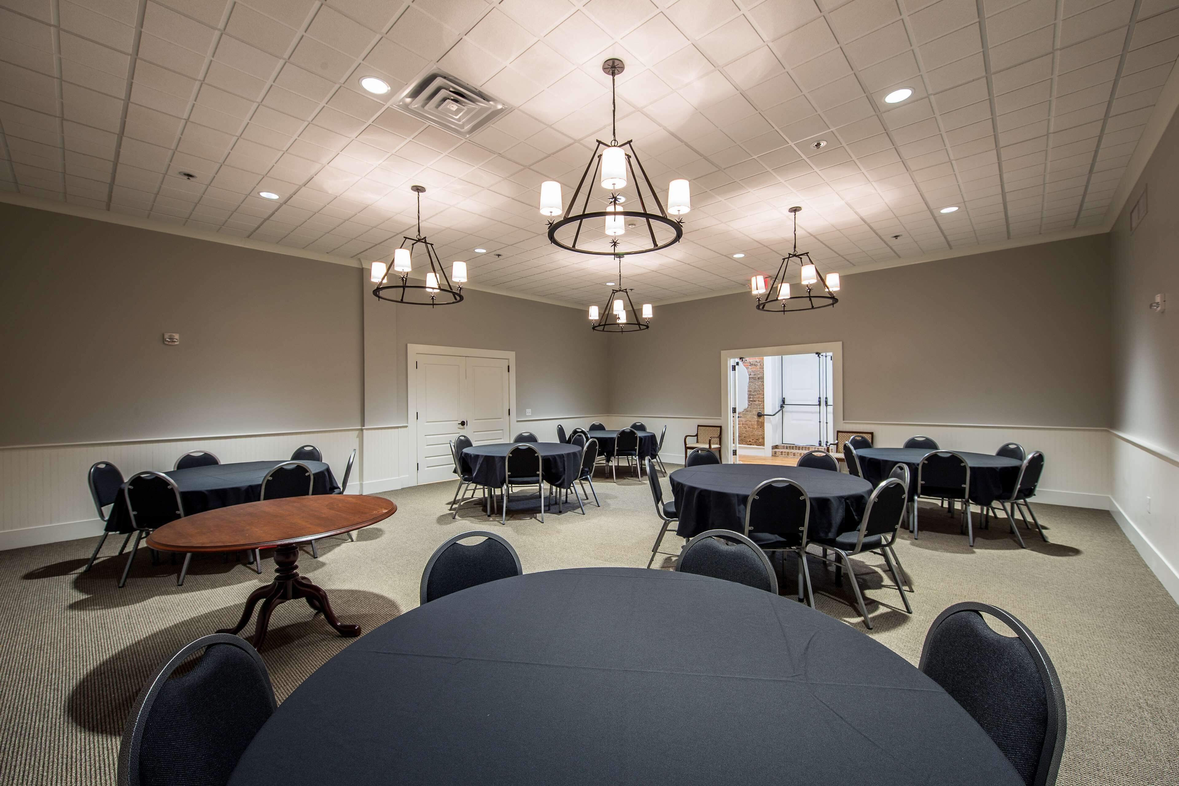 A conference room with round tables, chairs, and a wooden table in the center.
