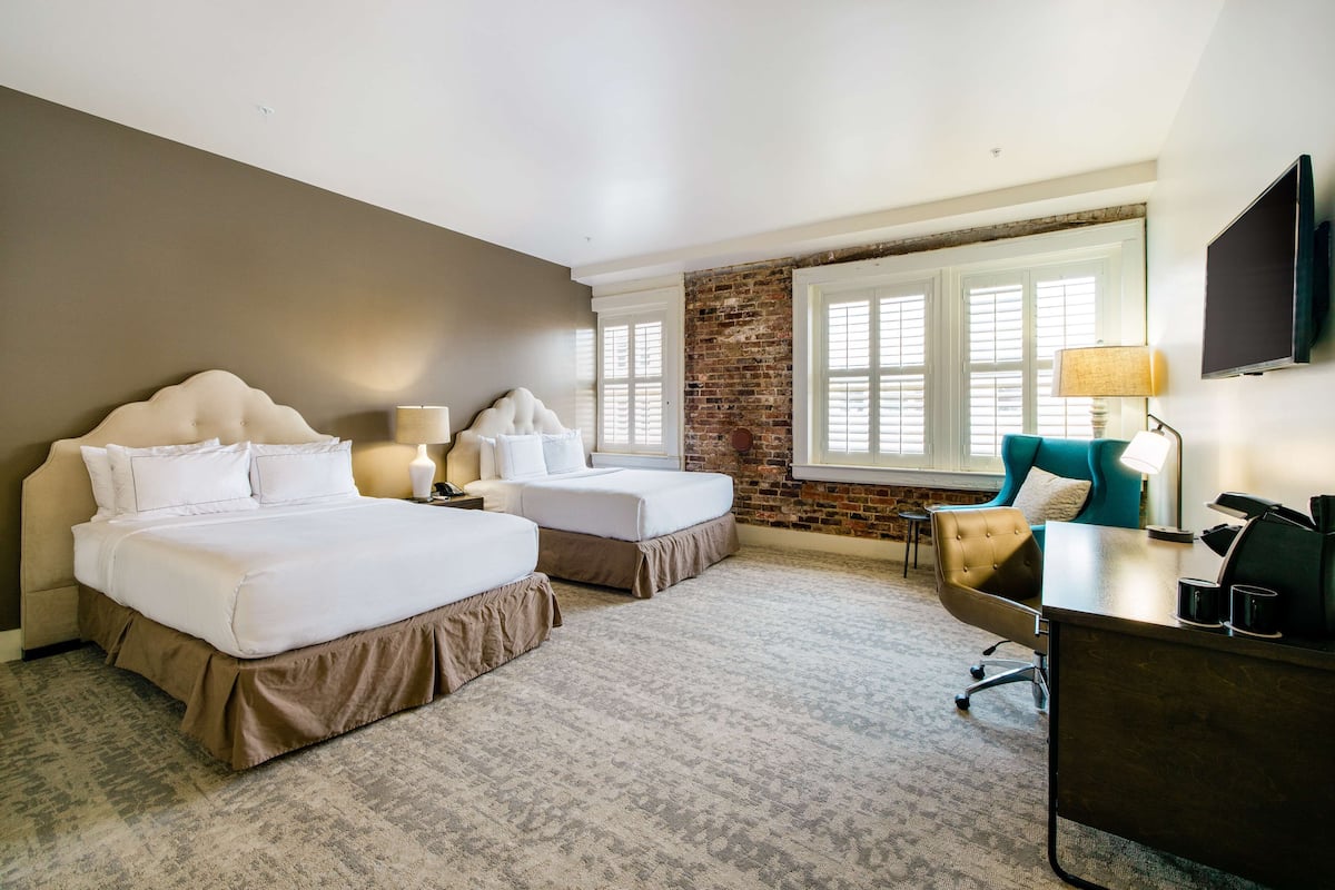 A hotel room with two beds, a desk, a chair, a TV, and a window with blinds.