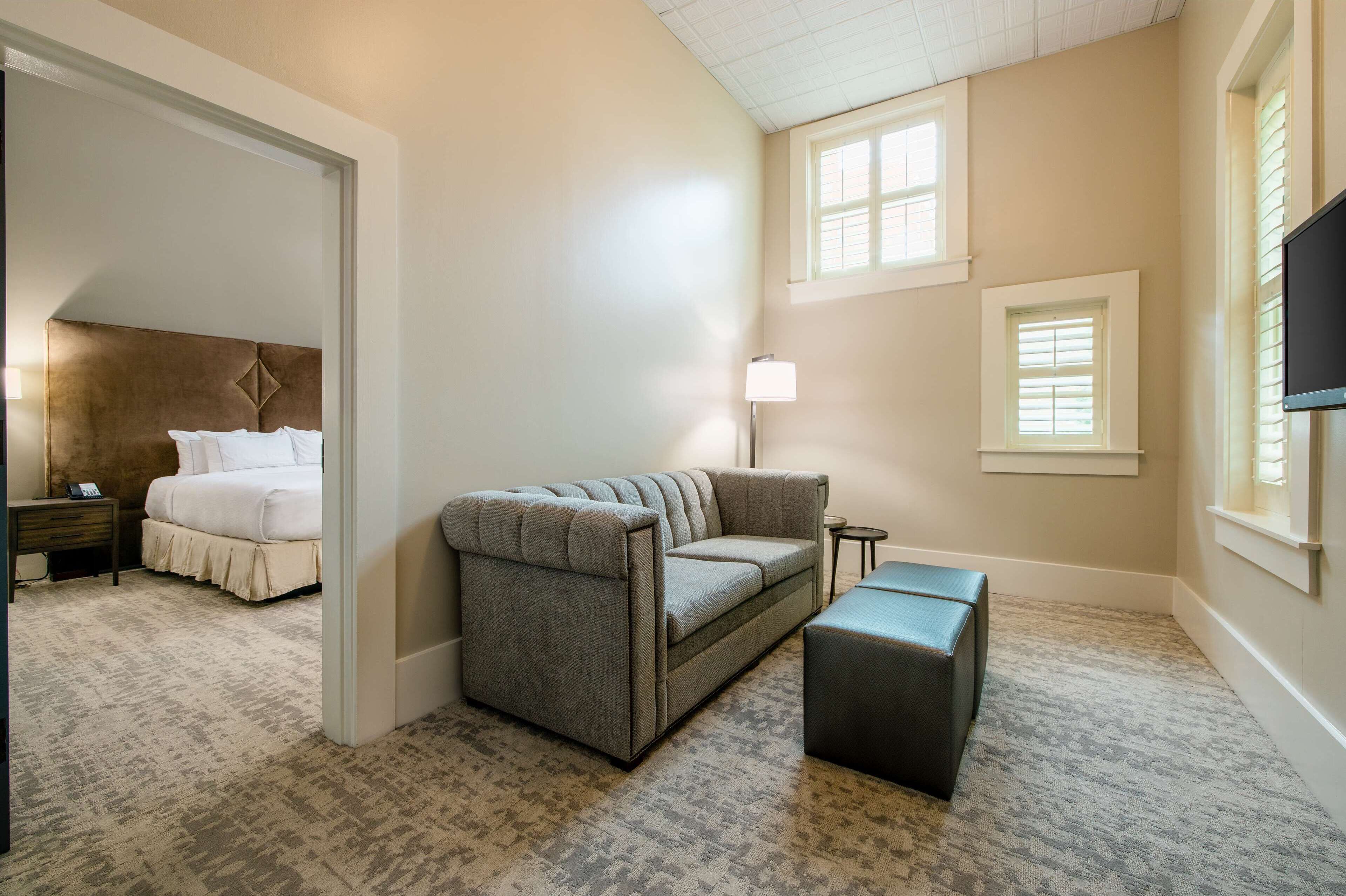 A bedroom with a bed, a gray sofa, a small table, and a TV.
