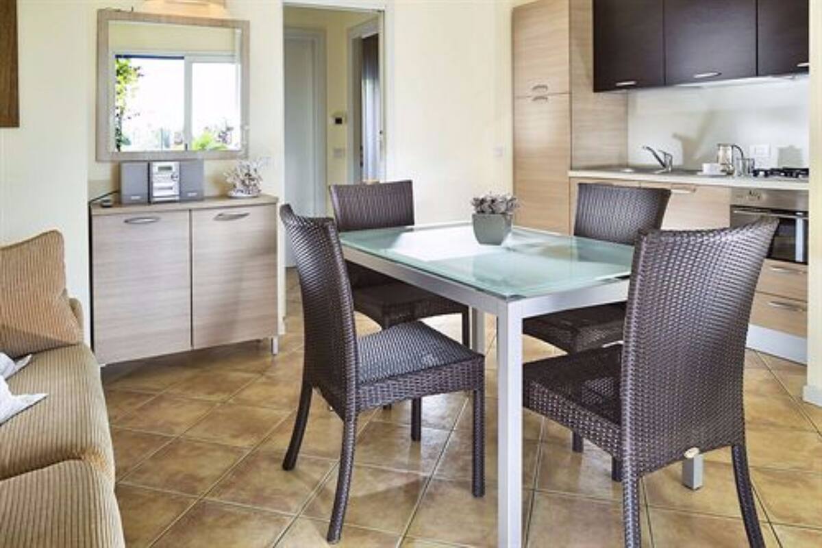 A modern kitchen with a dining area, featuring a glass-top table, wicker chairs, and a built-in cabinet.