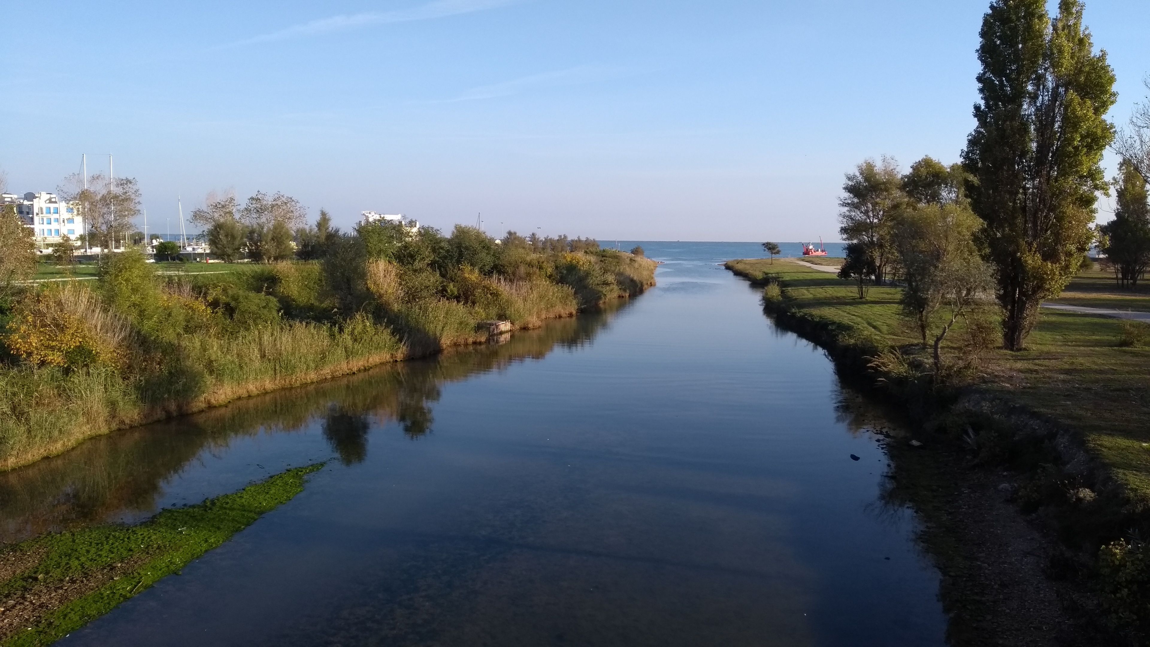 A calm river with a narrow path alongside, surrounded by greenery and trees.