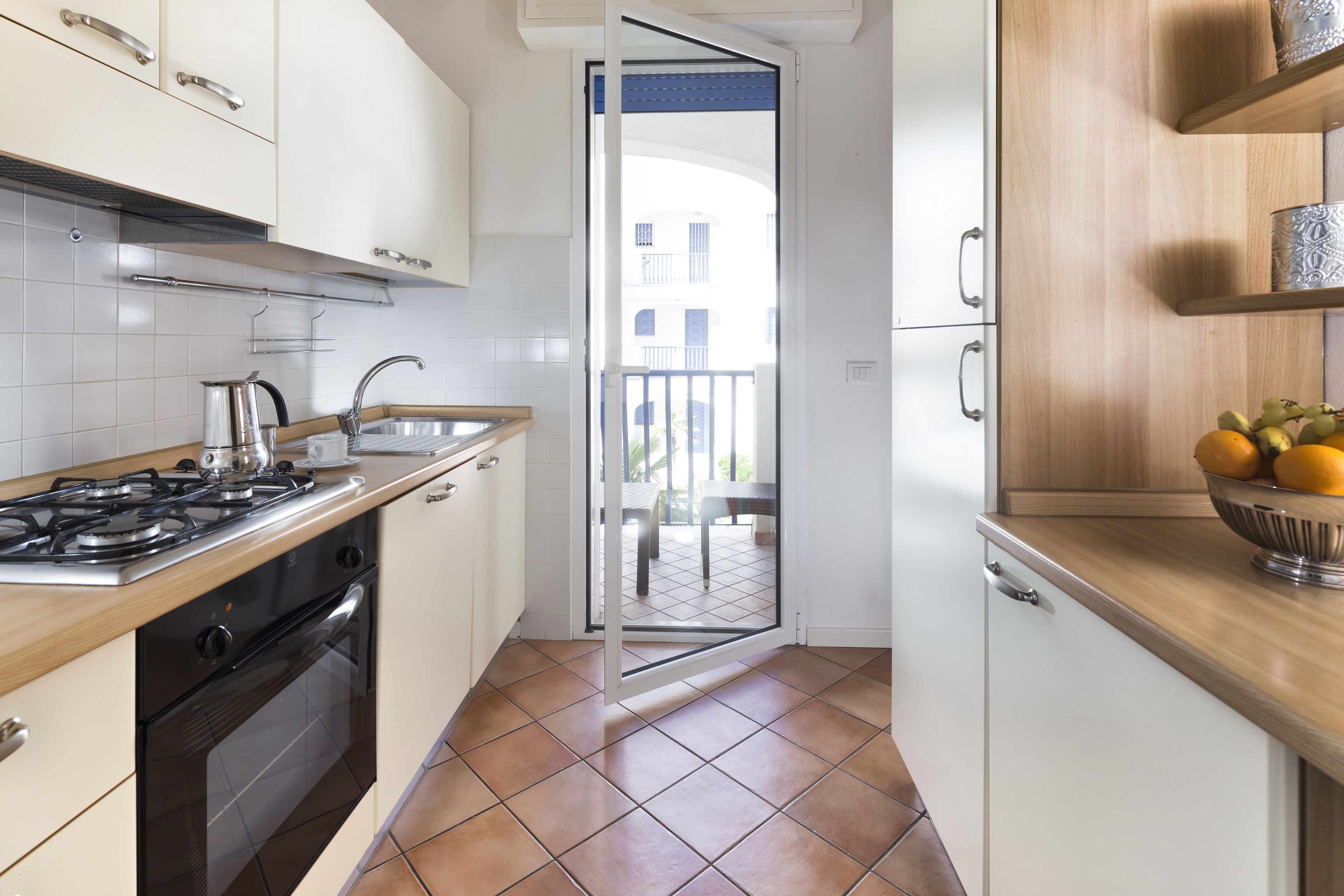 Una cocina con armarios blancos, una estufa a gas y vistas al balcón.